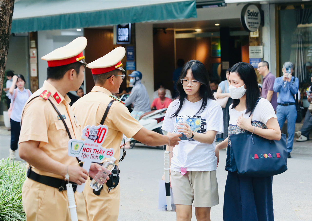 Cán bộ, chiến sĩ Công an Thủ đô phát nước uống, tài liệu ôn tập và quạt giấy cho thí sinh trước giờ vào phòng thi, thể hiện tinh thần đồng hành, sẻ chia trong mùa thi.